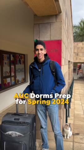 A smiling male student is holding his carry-on suitcase, text reads "AUC Dorms Prep for Spring 2024"