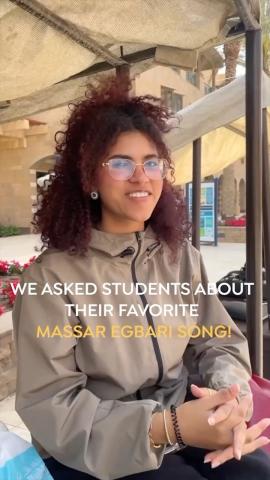 A girl is smiling  and wearing glasses. Text: We asked students about their favorite Massar Egbari song!