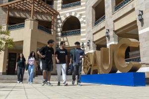 Male and female students walking next to big sized letters A U C