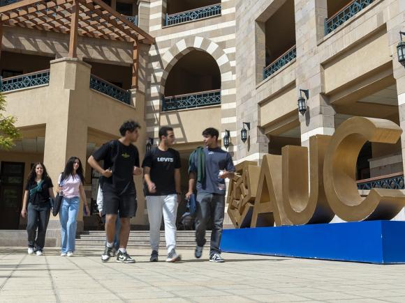 Male and female students walking next to big sized letters A U C