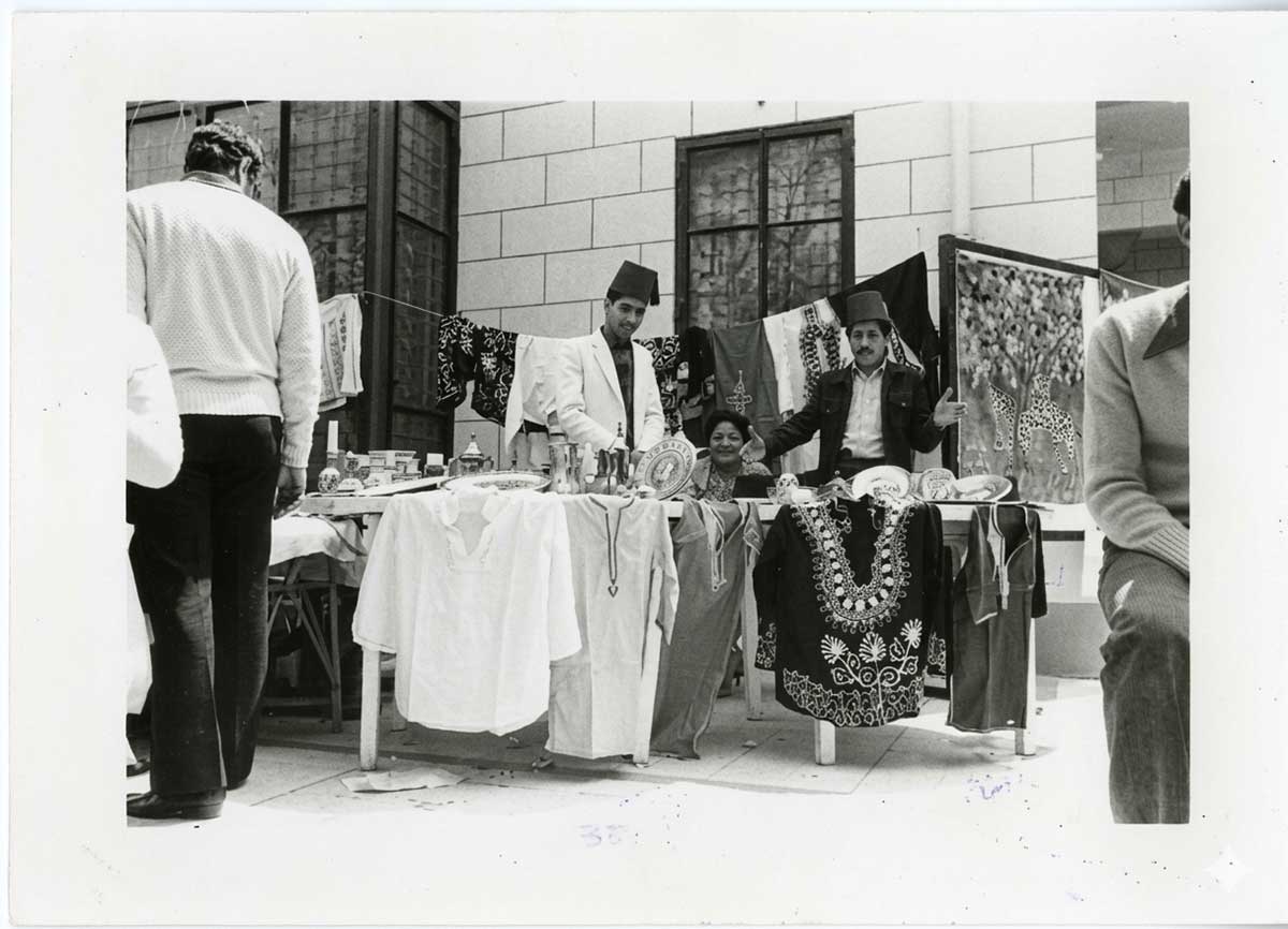 Three people display shirts at a stand in front of a building