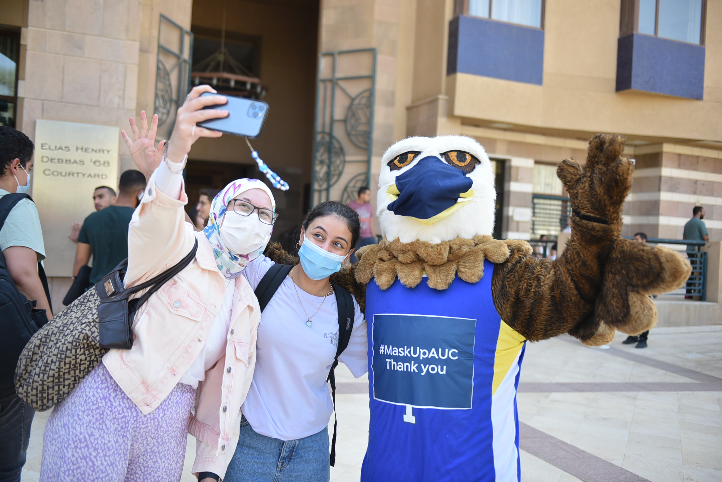 students taking a selfie with auc mascot and wearing masks 