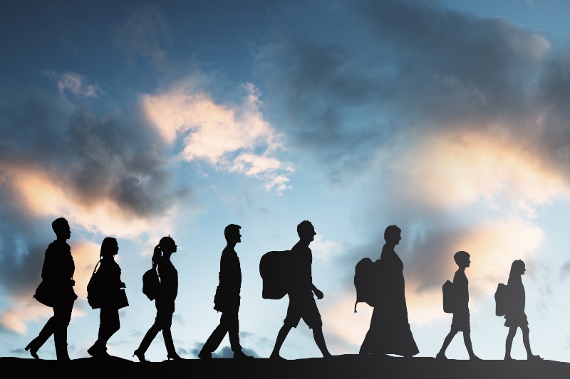 Silhouette of people walking in a line with the sky illuminated behind them