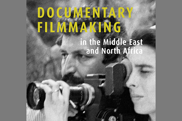 A black and white book cover with a man in the background standing  next to a woman looking through a camera in the foreground.