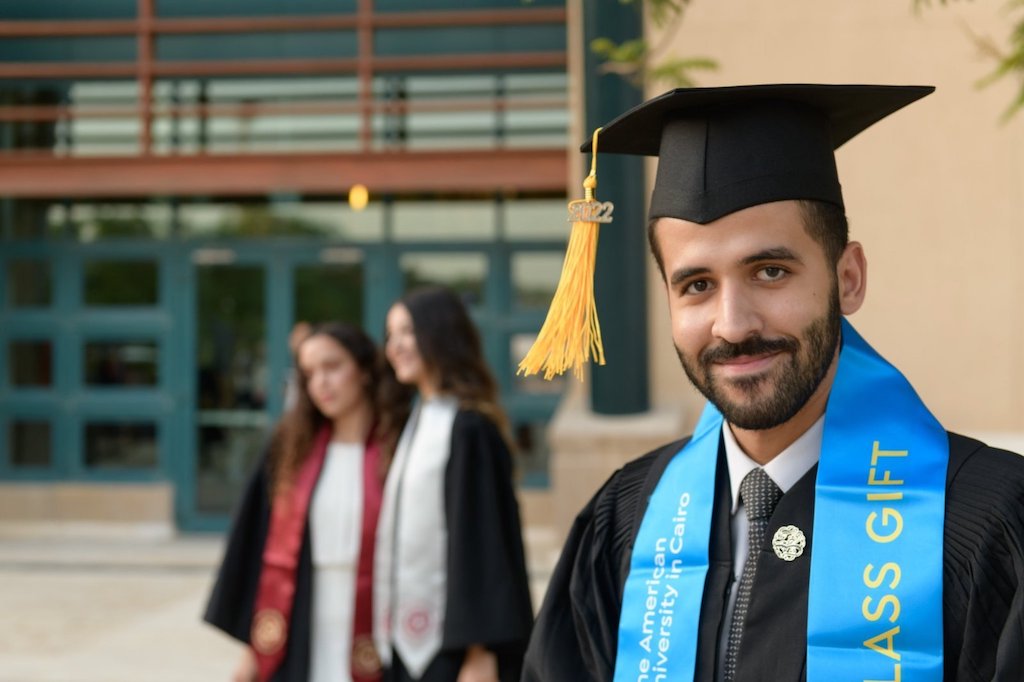 Male student in cap and gown and wearing a blue sash