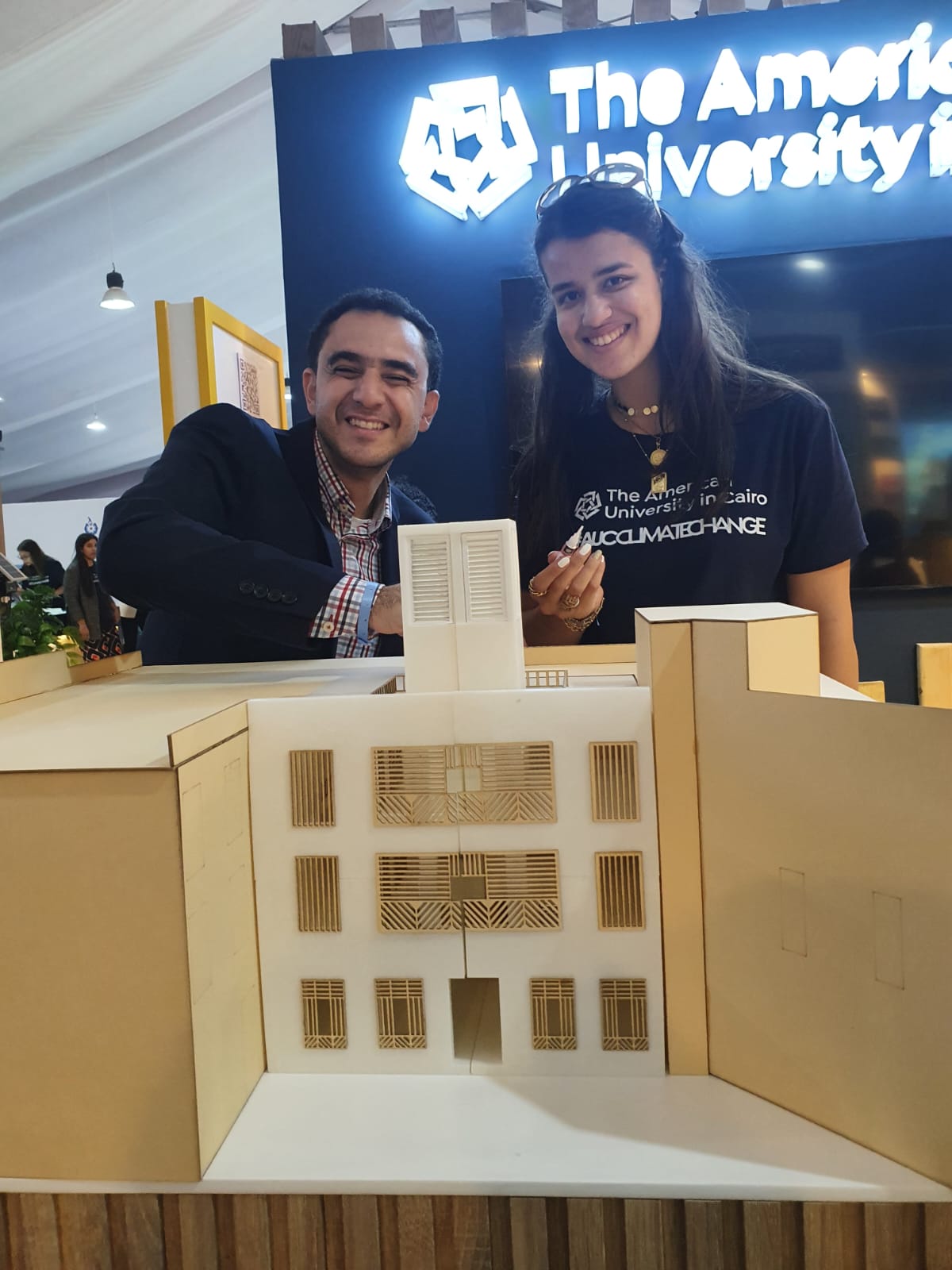 A man and a female student smiling in front of a model of a building