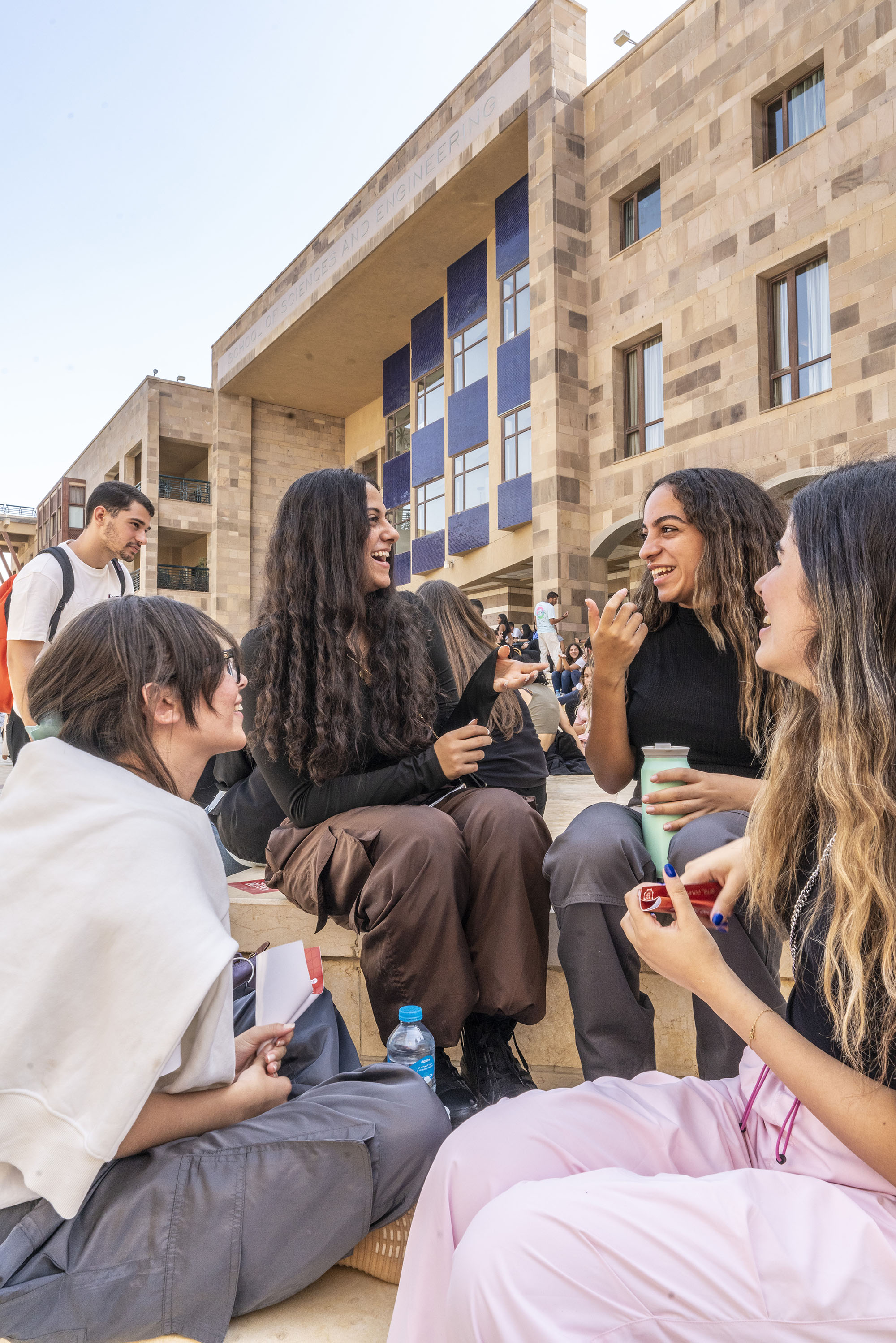 Students sitting in stairs under a building outdoors laughing 