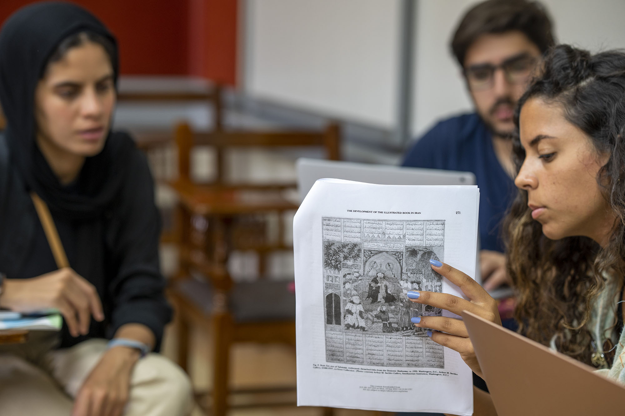 A girl holding a paper explaing to other students in a classroom