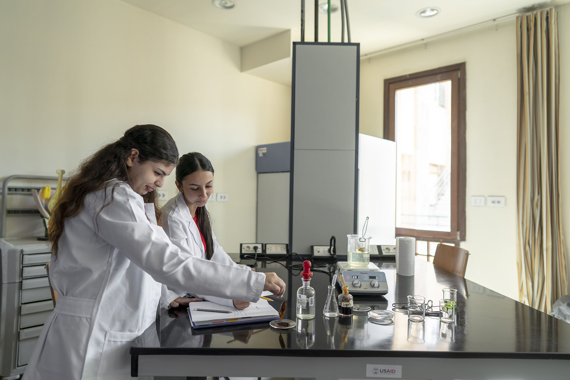 two girls wearing white lab coat conducting an experiment in a lab