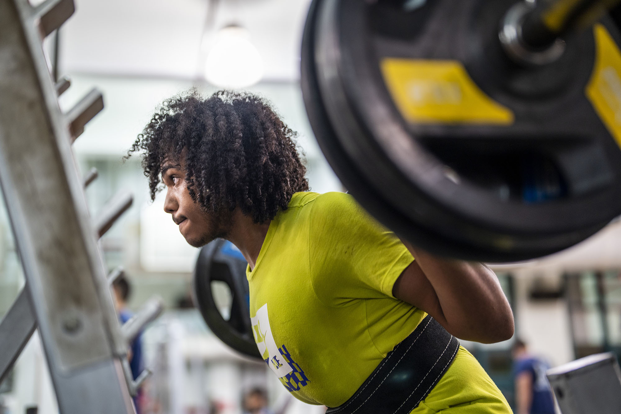 Male student lifting weights in the gym and wearing a wide belt on his waist