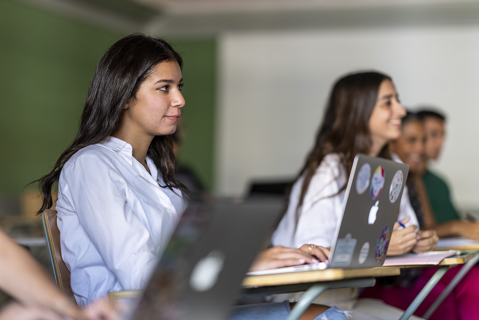 A girl in classroom sitting on a desk with a laptop in fornt  of her 