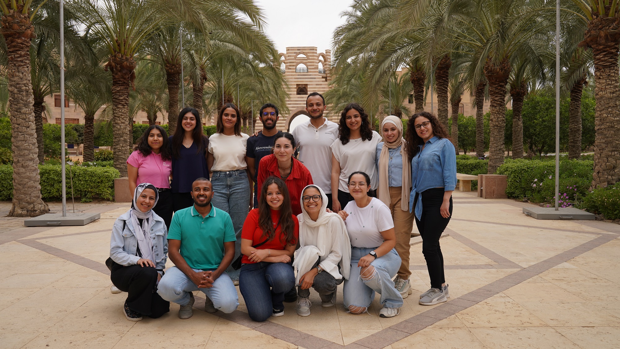 Group of male and female students standing next to palm trees in front of a portal