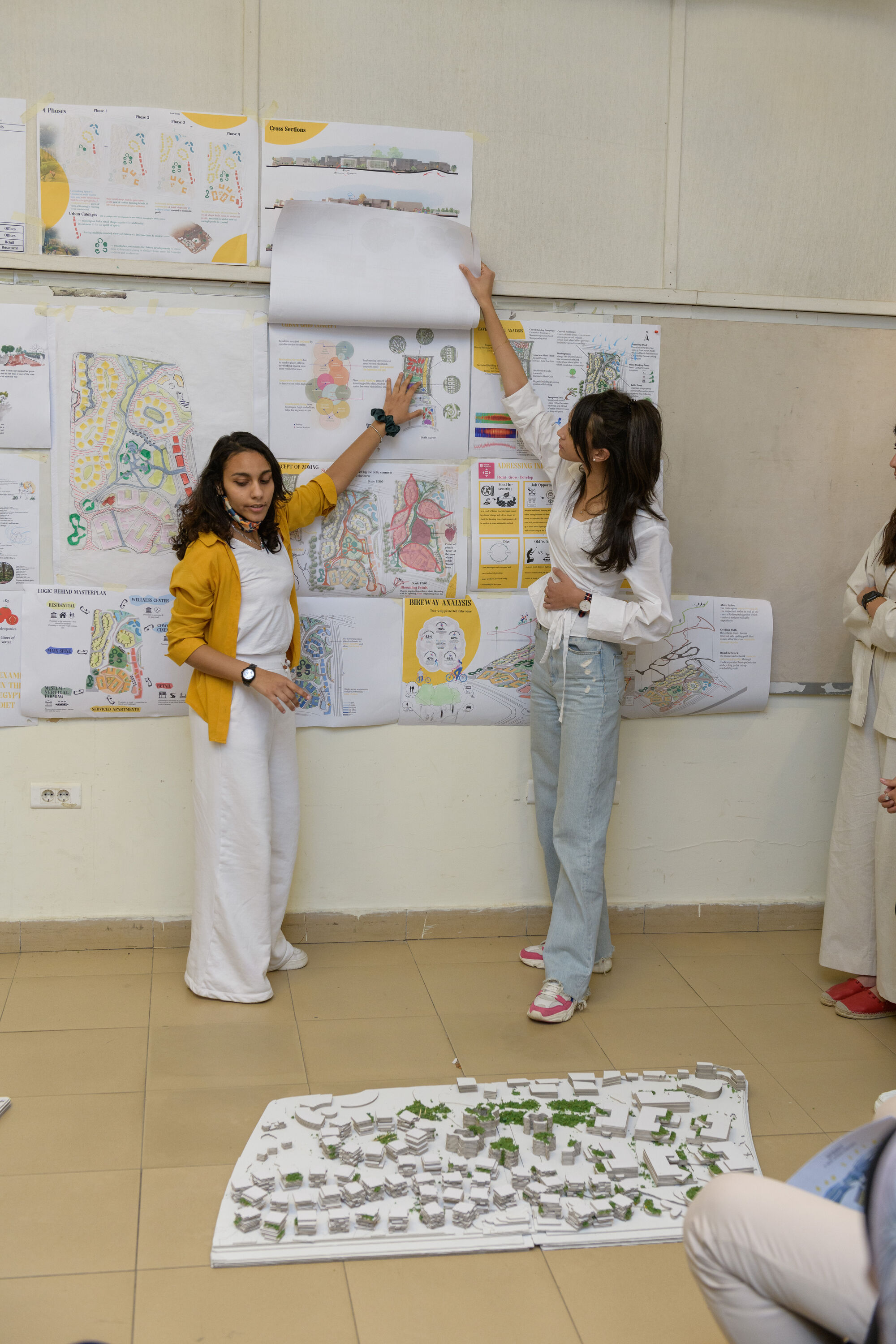 Vertical picture with two girls in a classroom pointing at their project on the board