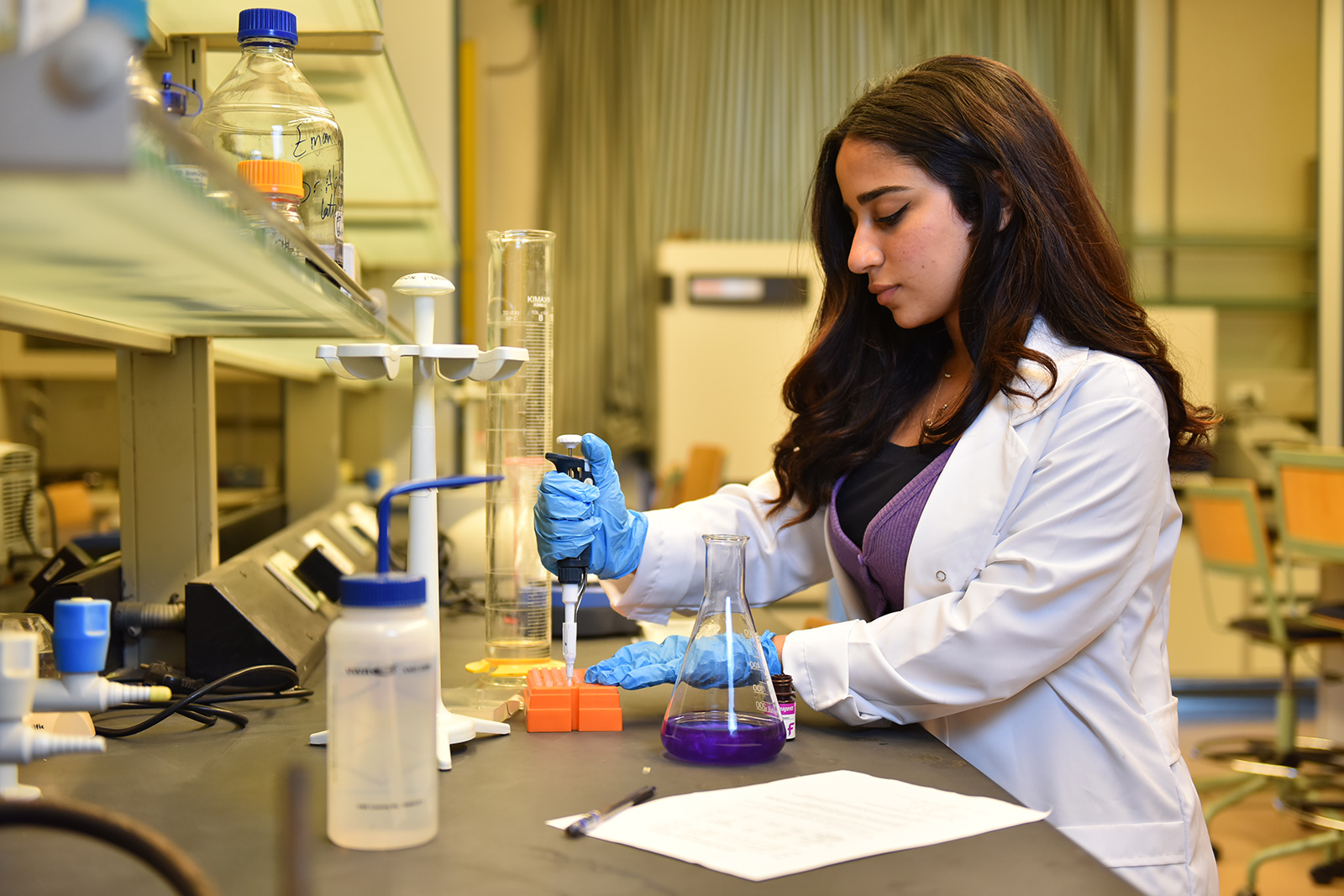 Side profile of a girl wearing a lab coat in a lab holding a tube