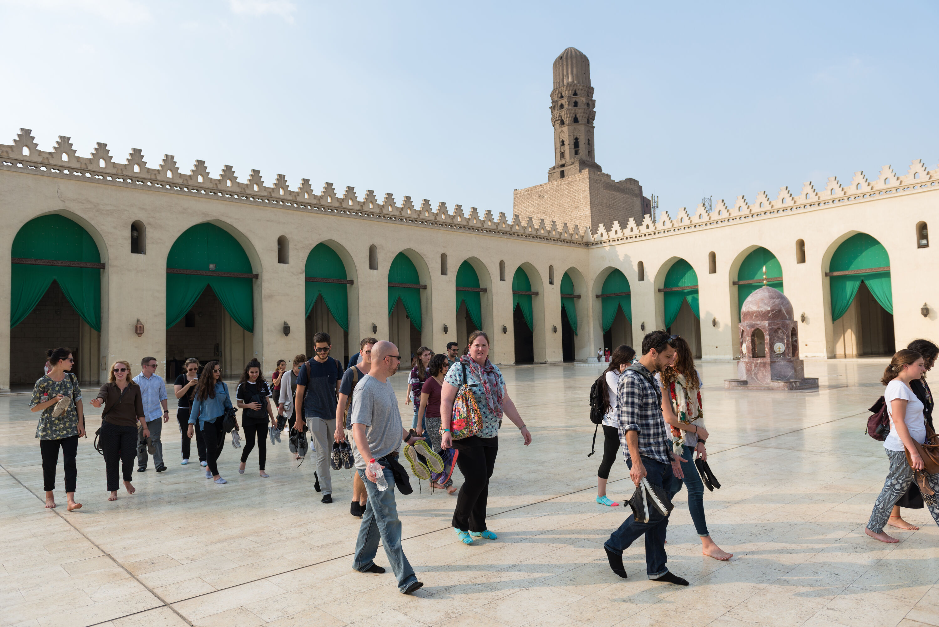 Group of international students walking in a mosque's open area holding their shoes