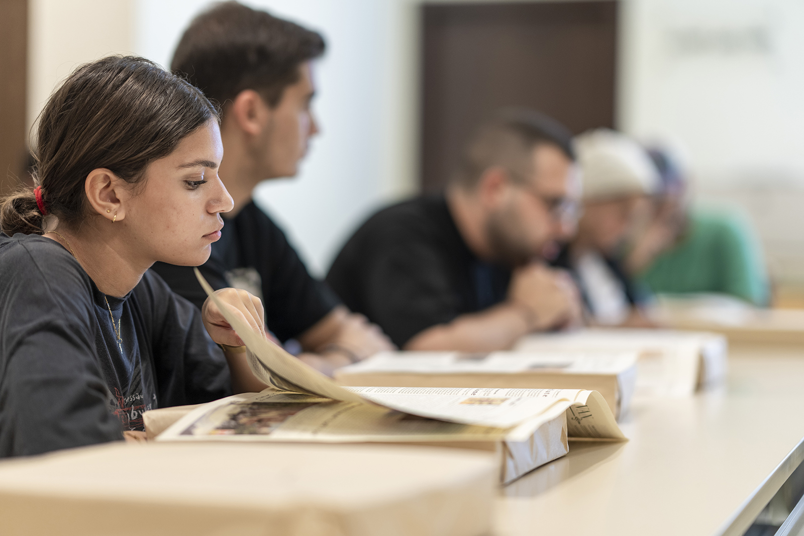 Girl sitting in a classroom flipping page of book infront of her