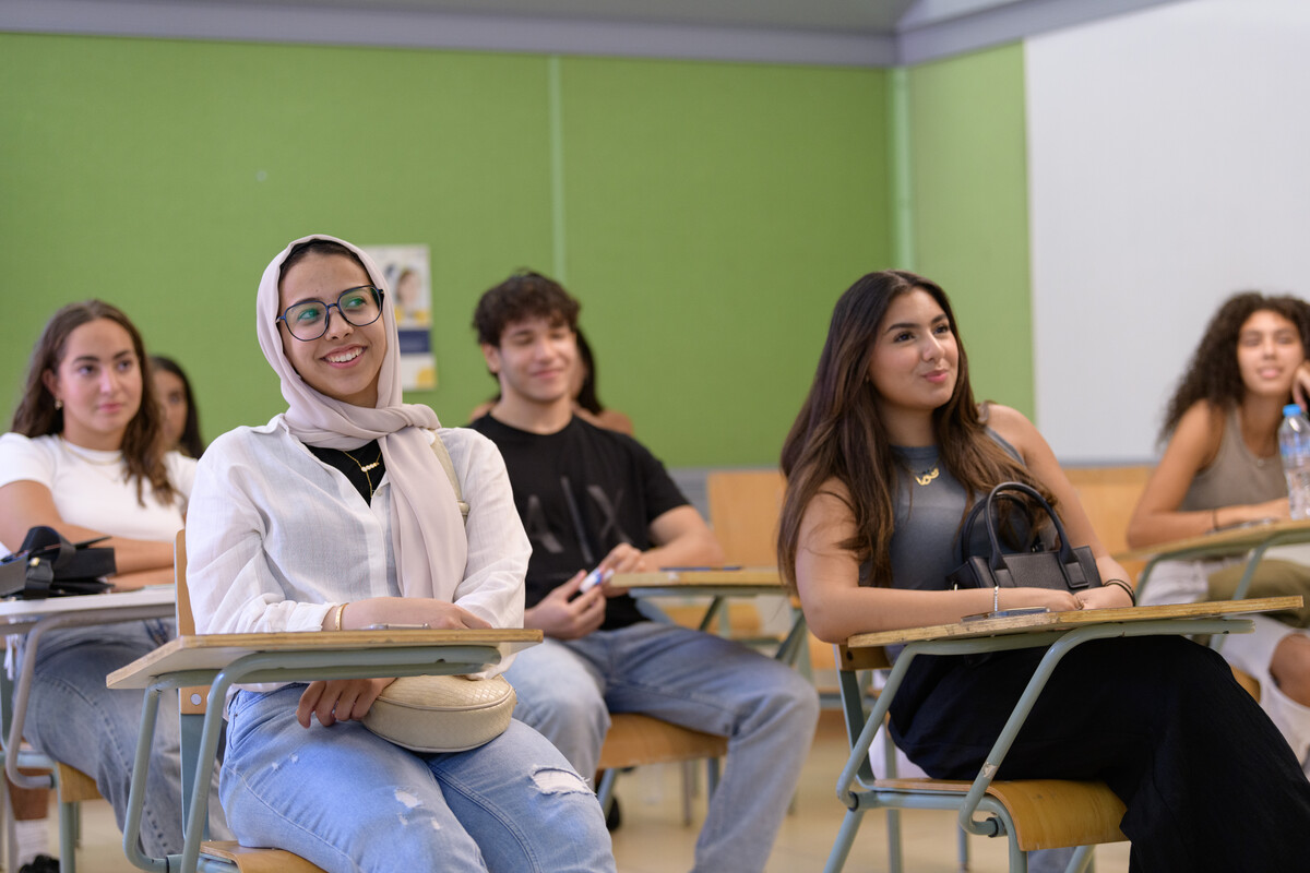 AUC students sit at desks in a classroom with a green wall behind them