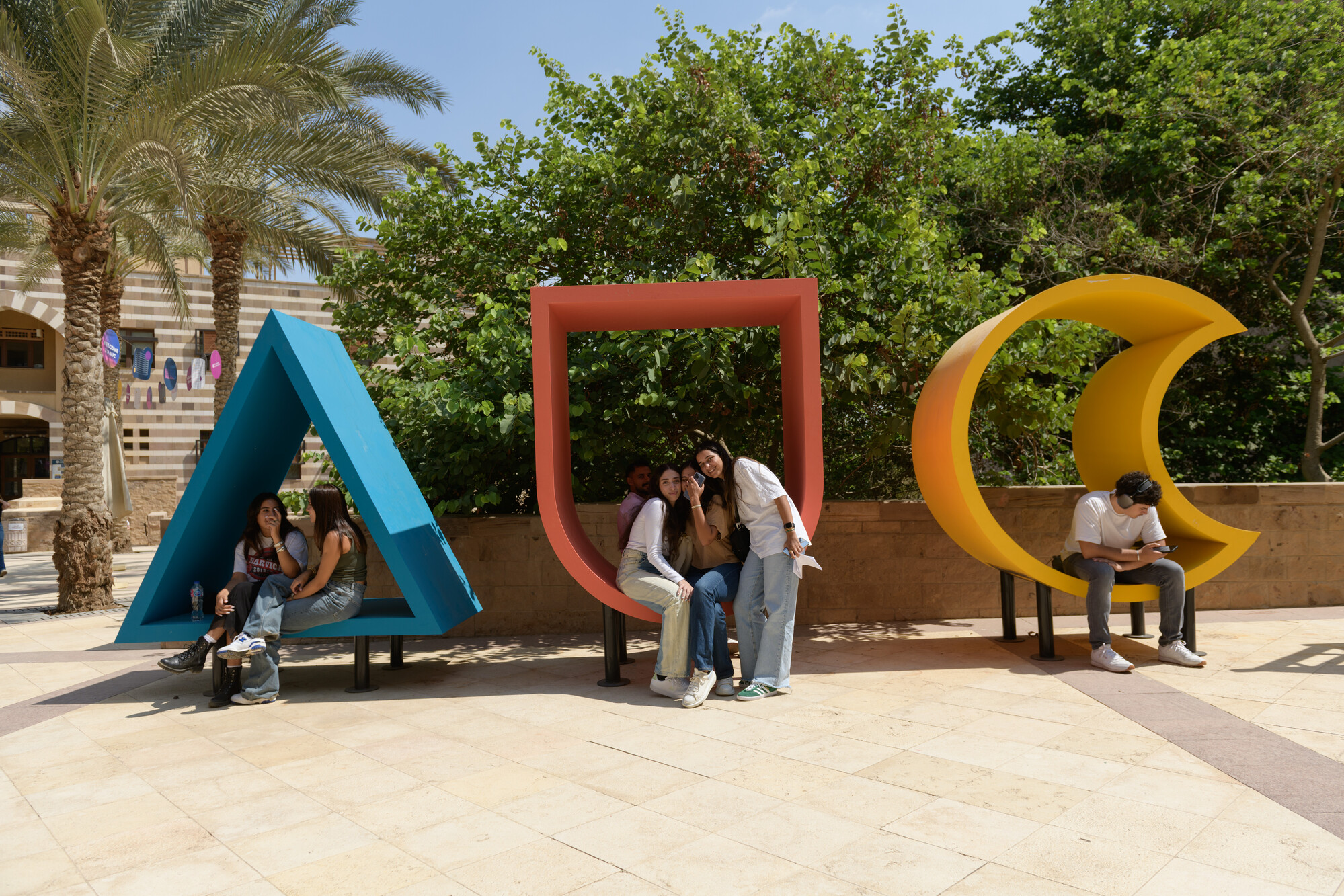 Girls sitting in a big letter figurine on campus