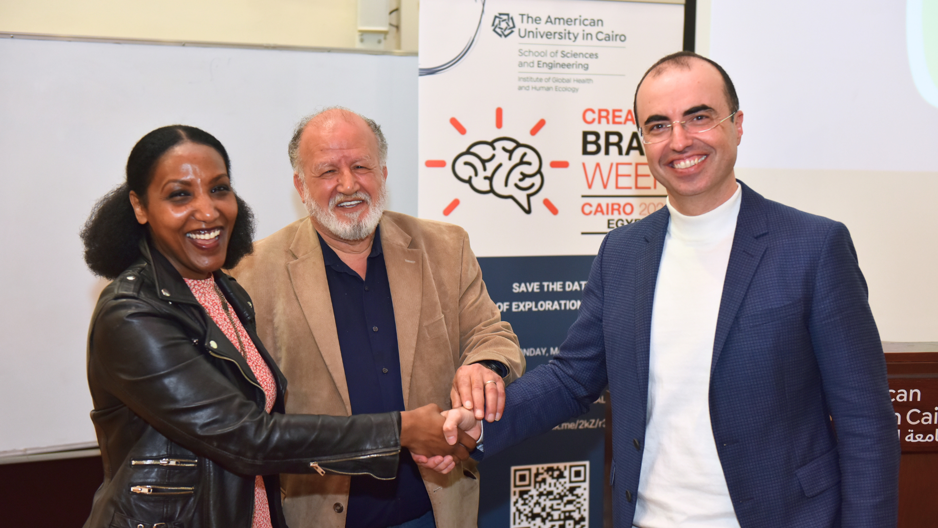 Two men and a woman shake hands in front of a background from Brain Week 2024