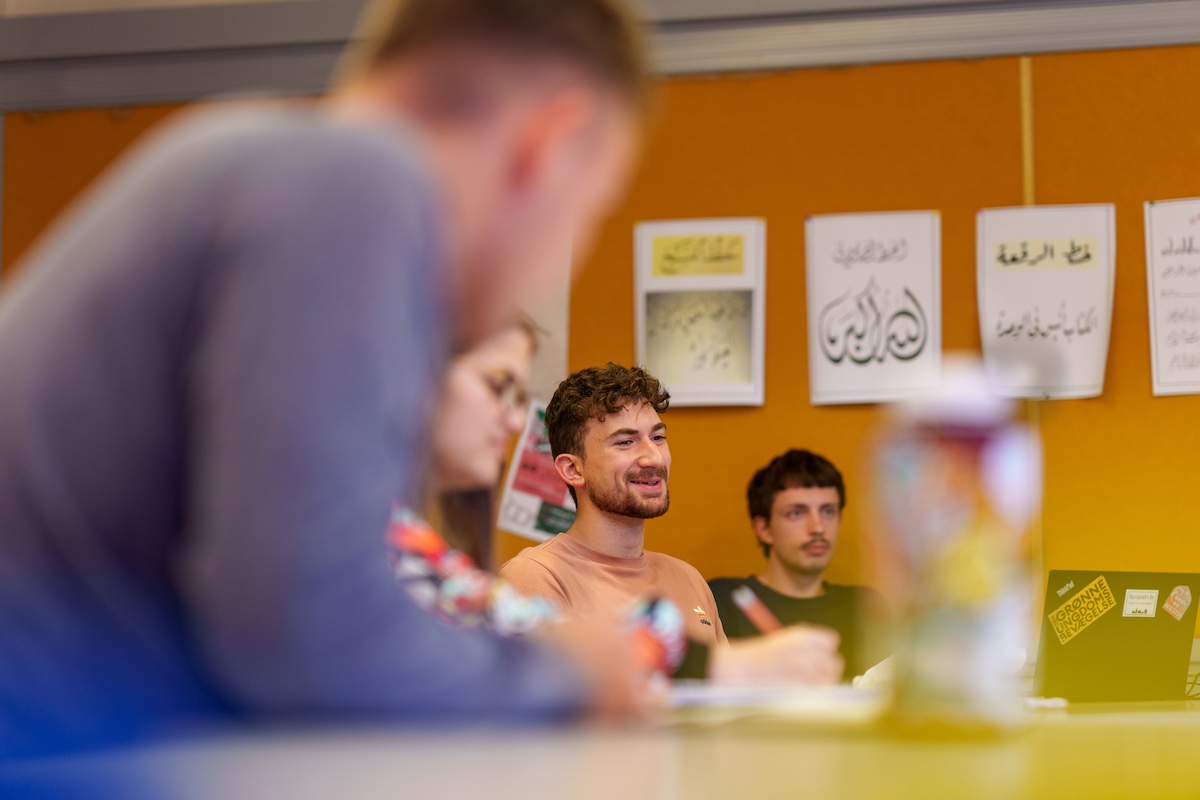 Students seated in a classroom, with Arabic calligraphy posters displayed on the wall behind them.