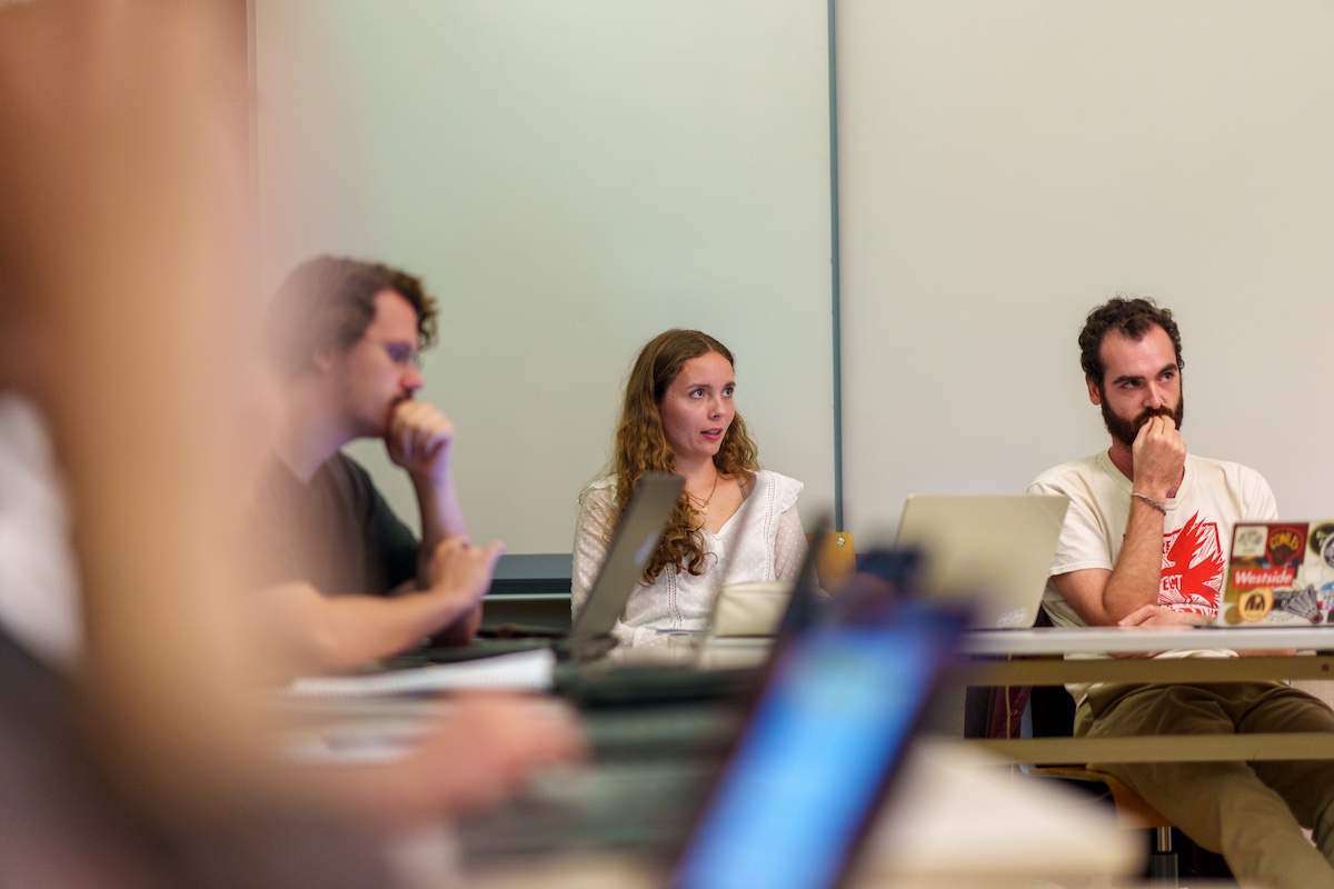 Students sit in a seminar-style classroom with laptops open.