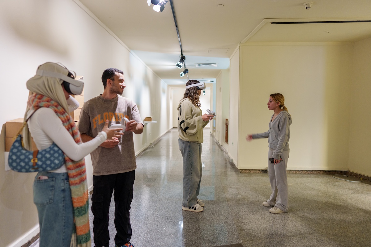 Two students wearing virtual reality headsets stand in a hallway while 2 other student guide the activity.