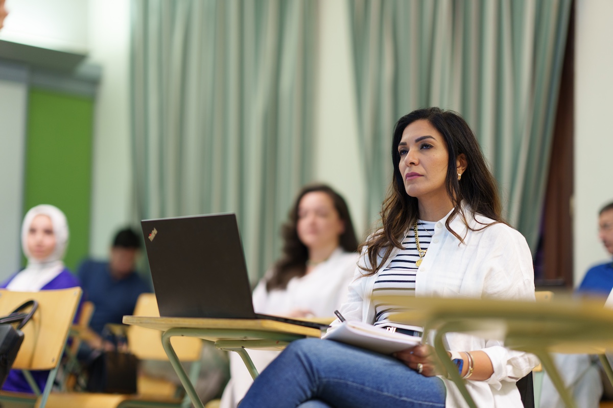 A student sits in a classroom with a laptop and notebook.