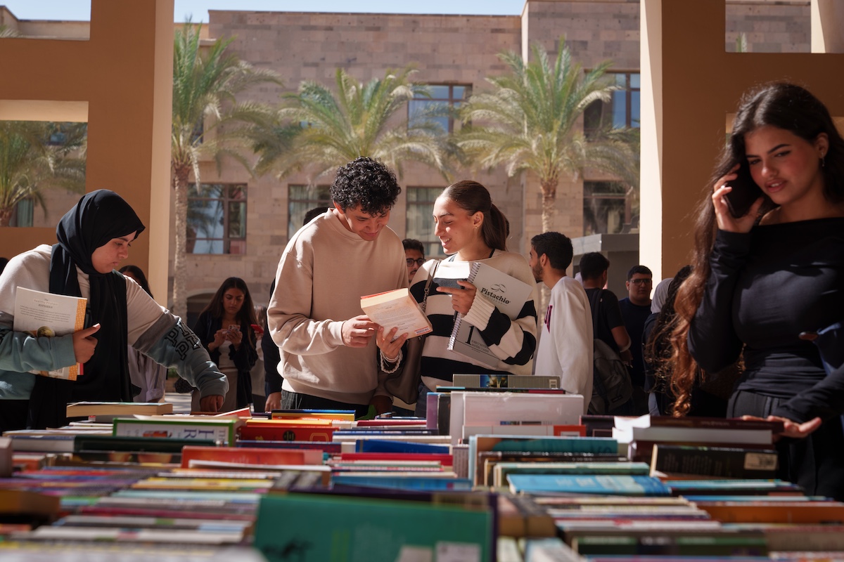 Students browse and exchange books at an outdoor book fair on campus.