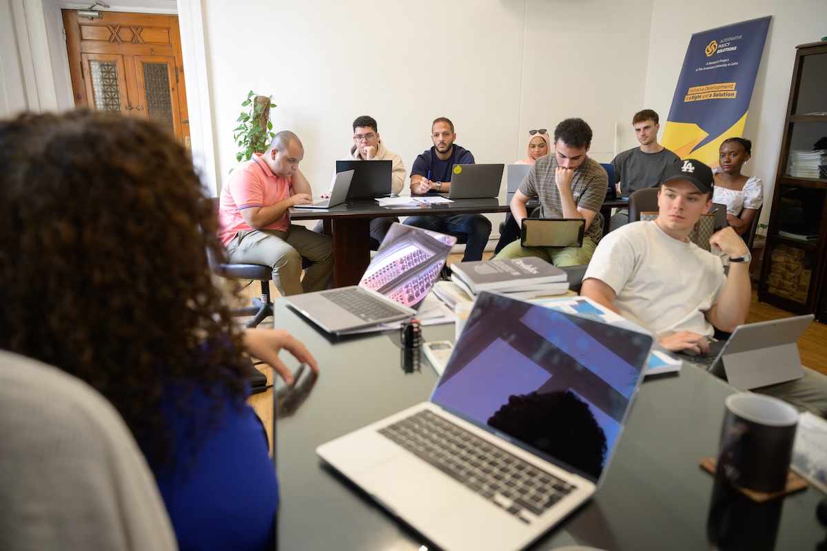 Students sit in a classroom with laptops open, listening to each other during a small group session.