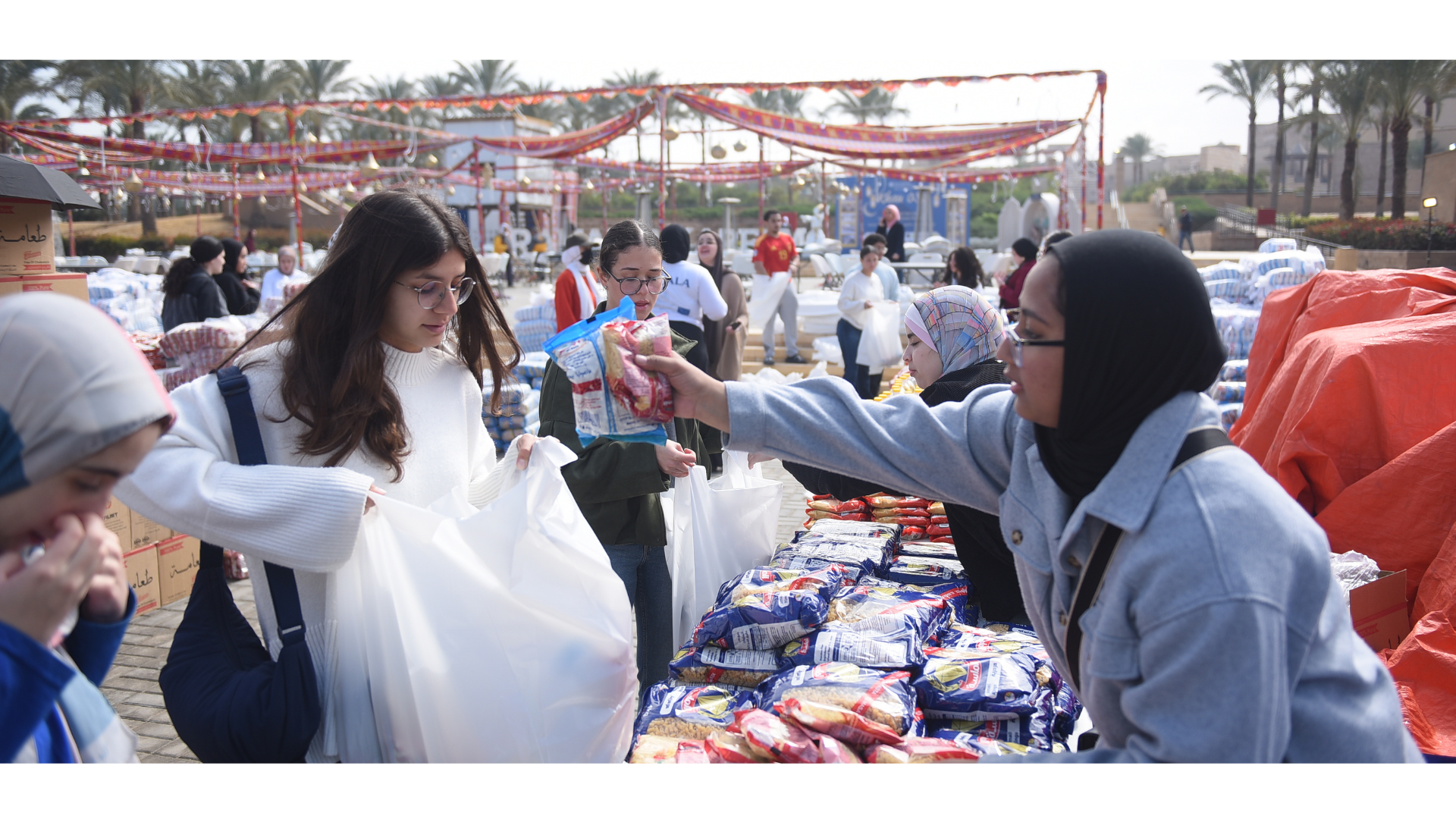 A young woman places bagged goods into a plastic bag of another young woman.