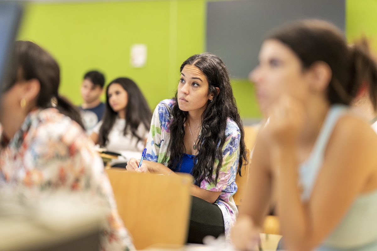 A student listens attentively while taking notes during a classroom lecture.