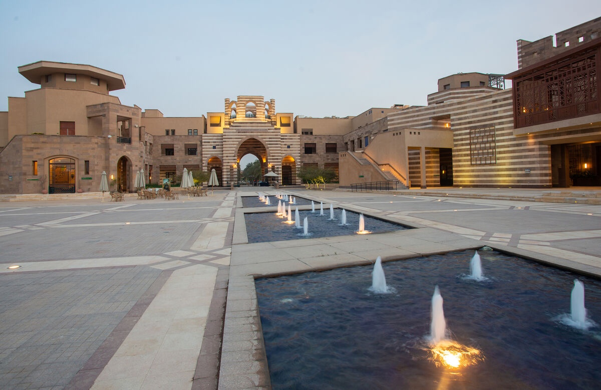 Open courtyard at AUC featuring fountains, stone buildings, and a large archway.