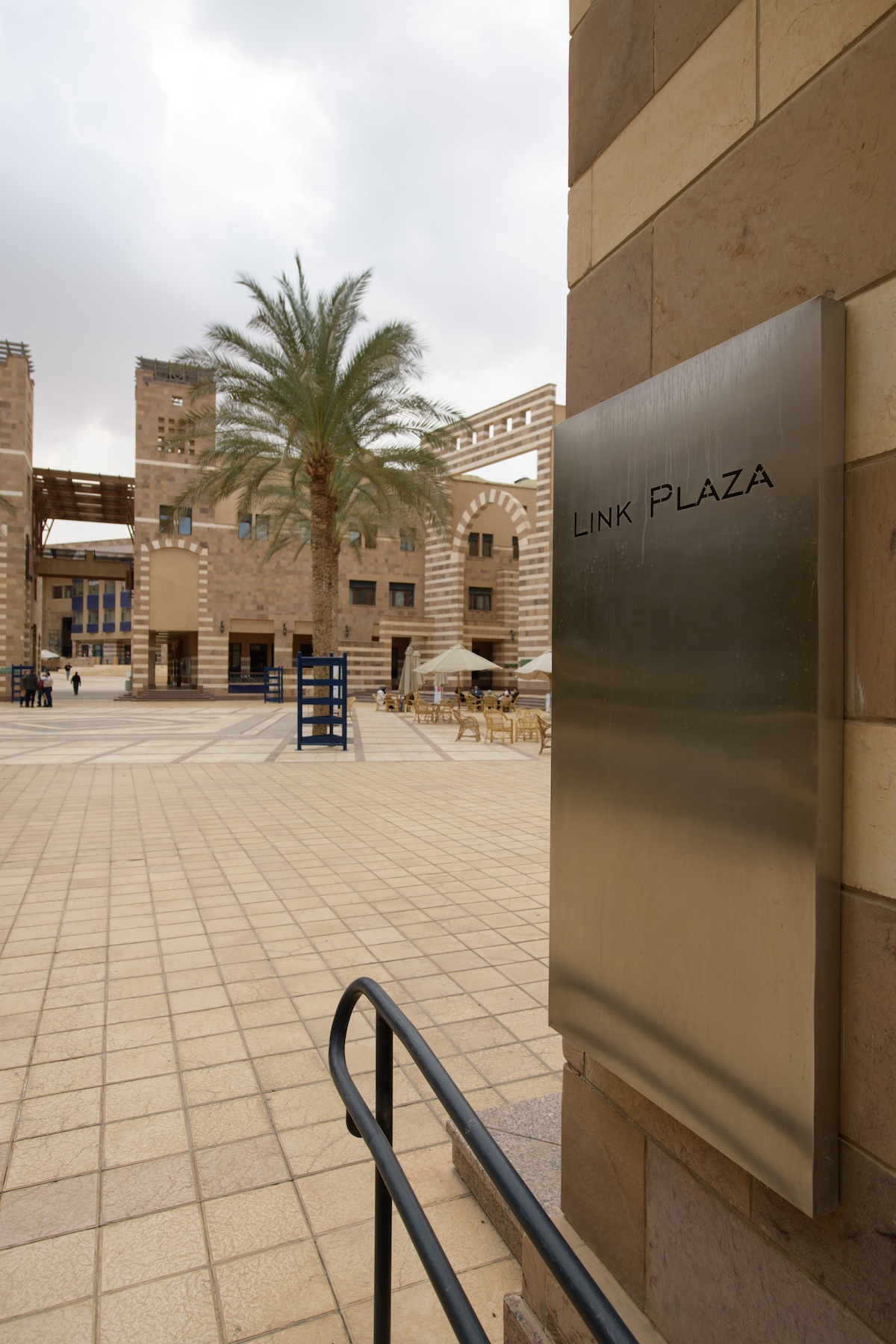 Campus view of Link Plaza with stone buildings, palm trees, and outdoor seating areas.