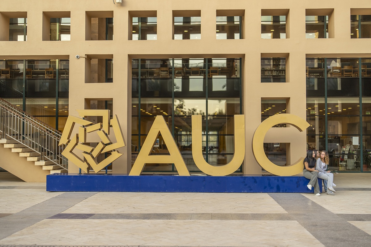 Students sitting next to the AUC big letters in front of a building
