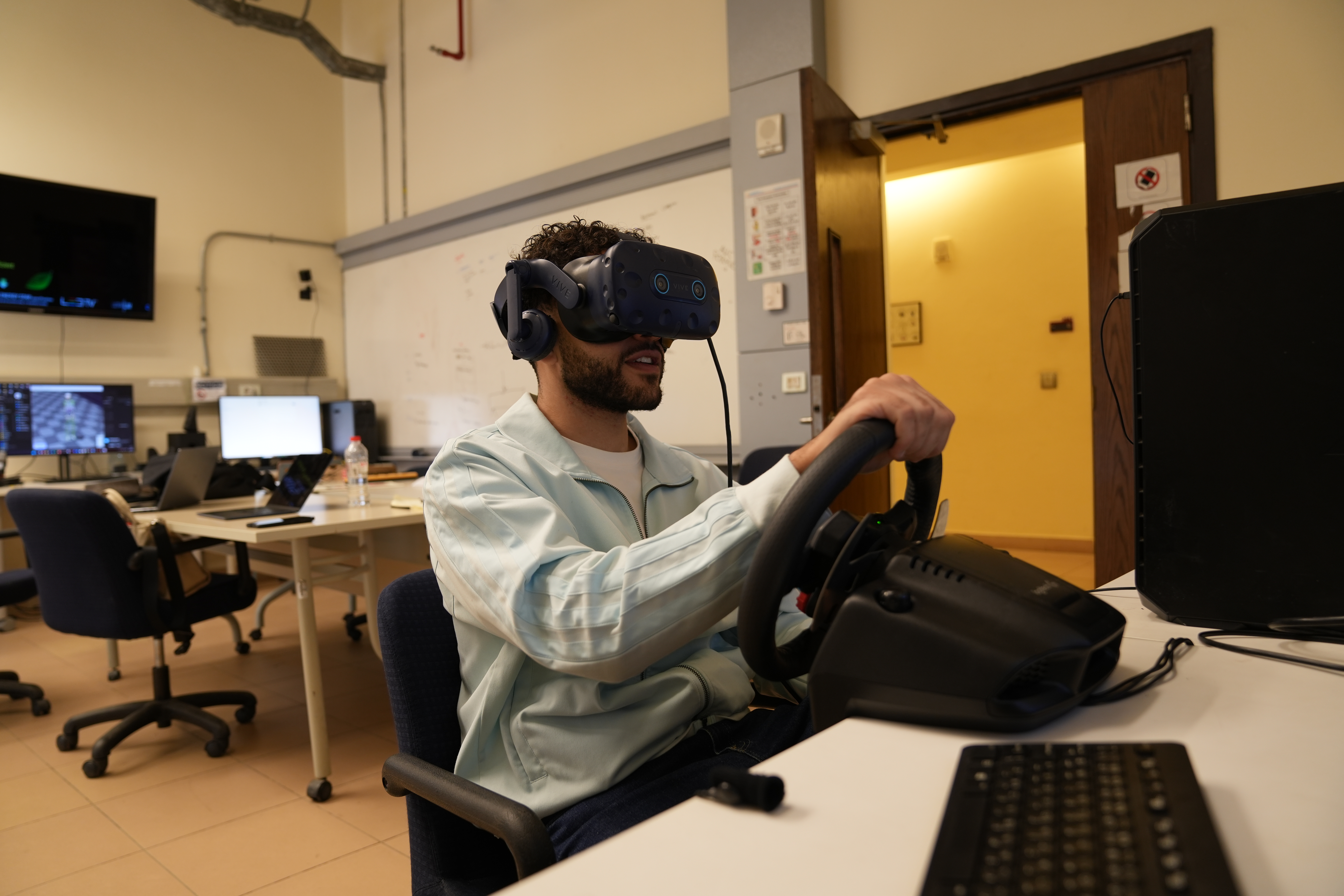 A person moves a steering wheel in a lab while wearing a vr headset