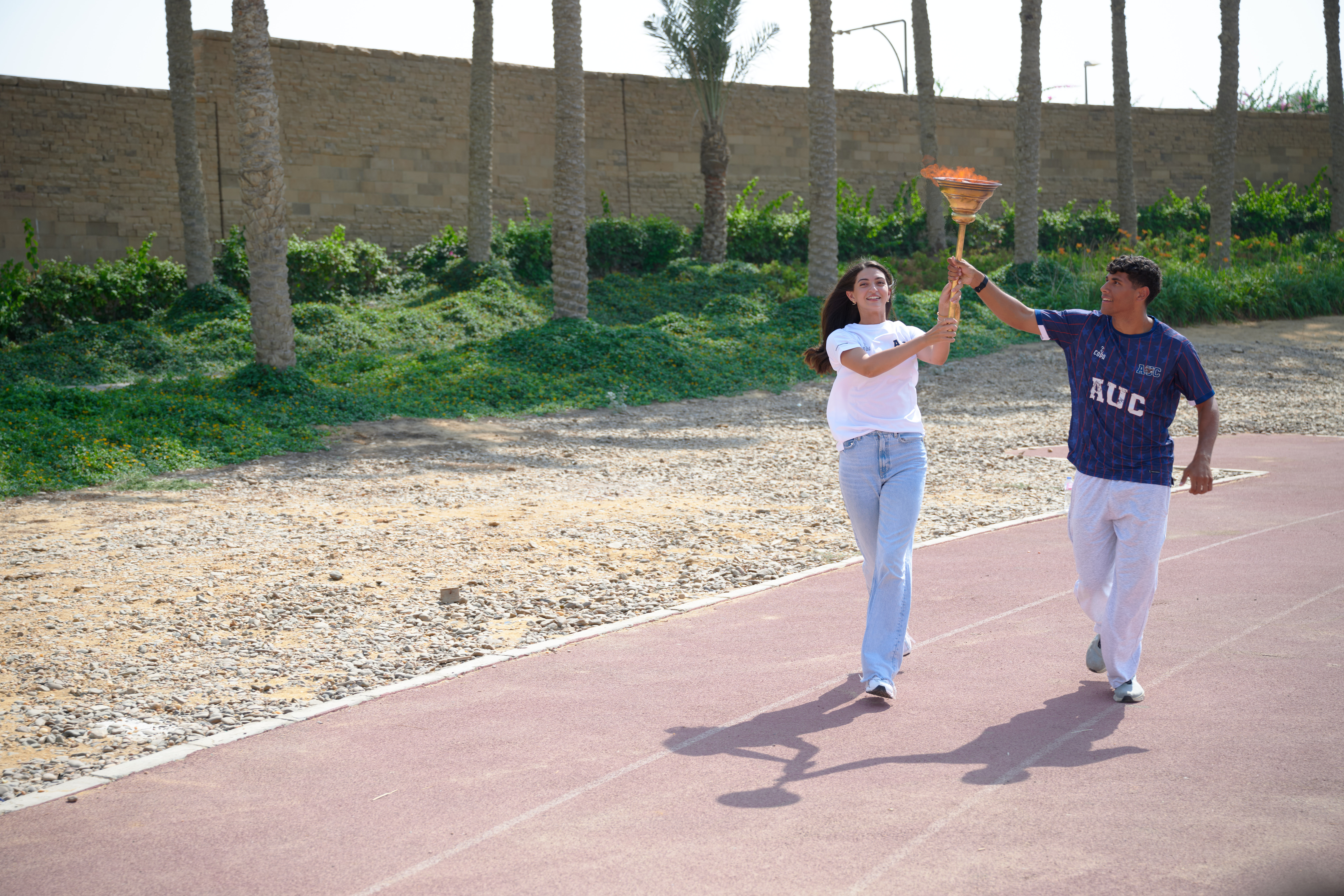 Two students holding the torch while running on track