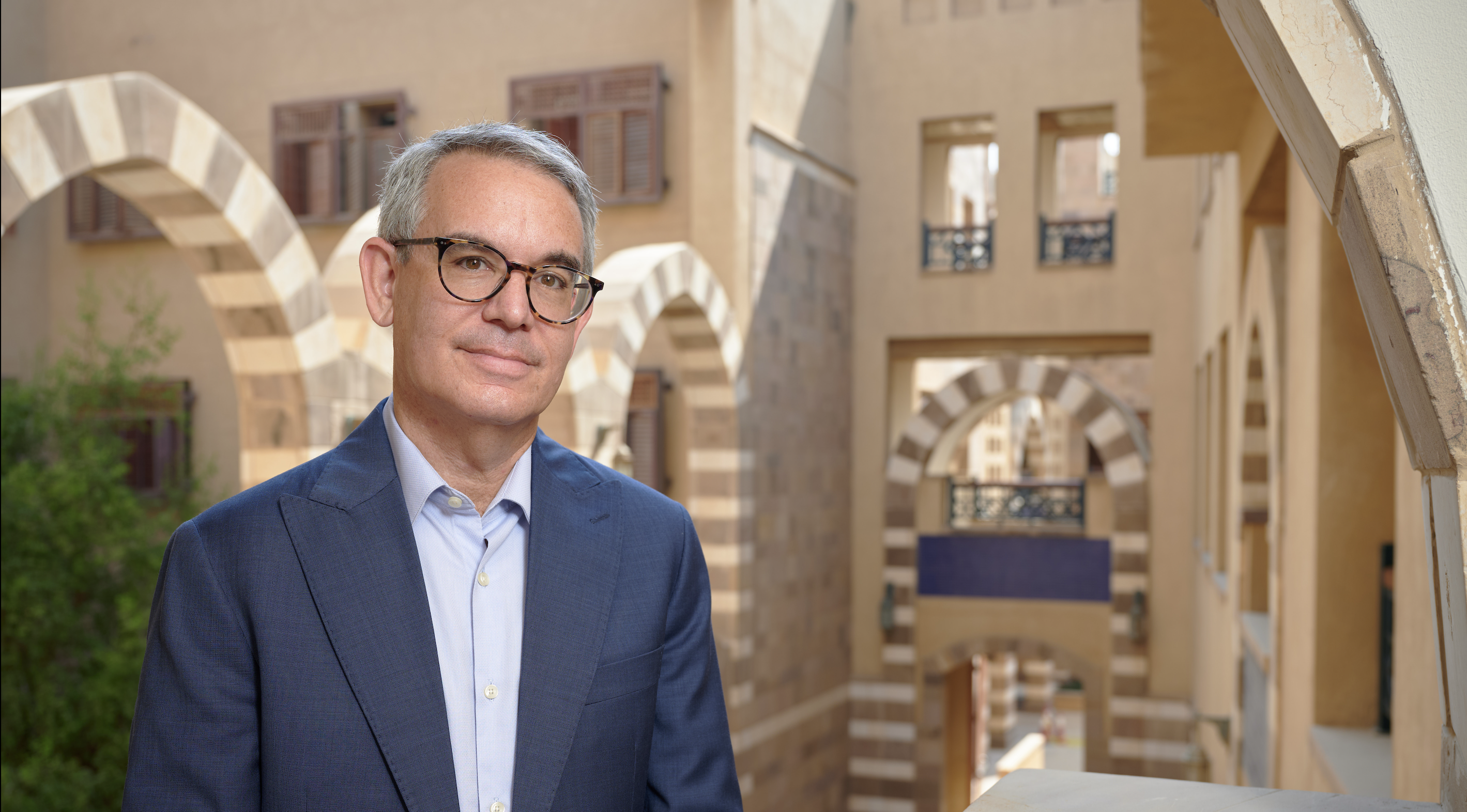 a man wearing a suit and glasses, standing in the architecturally hollow space inside the HUSS building