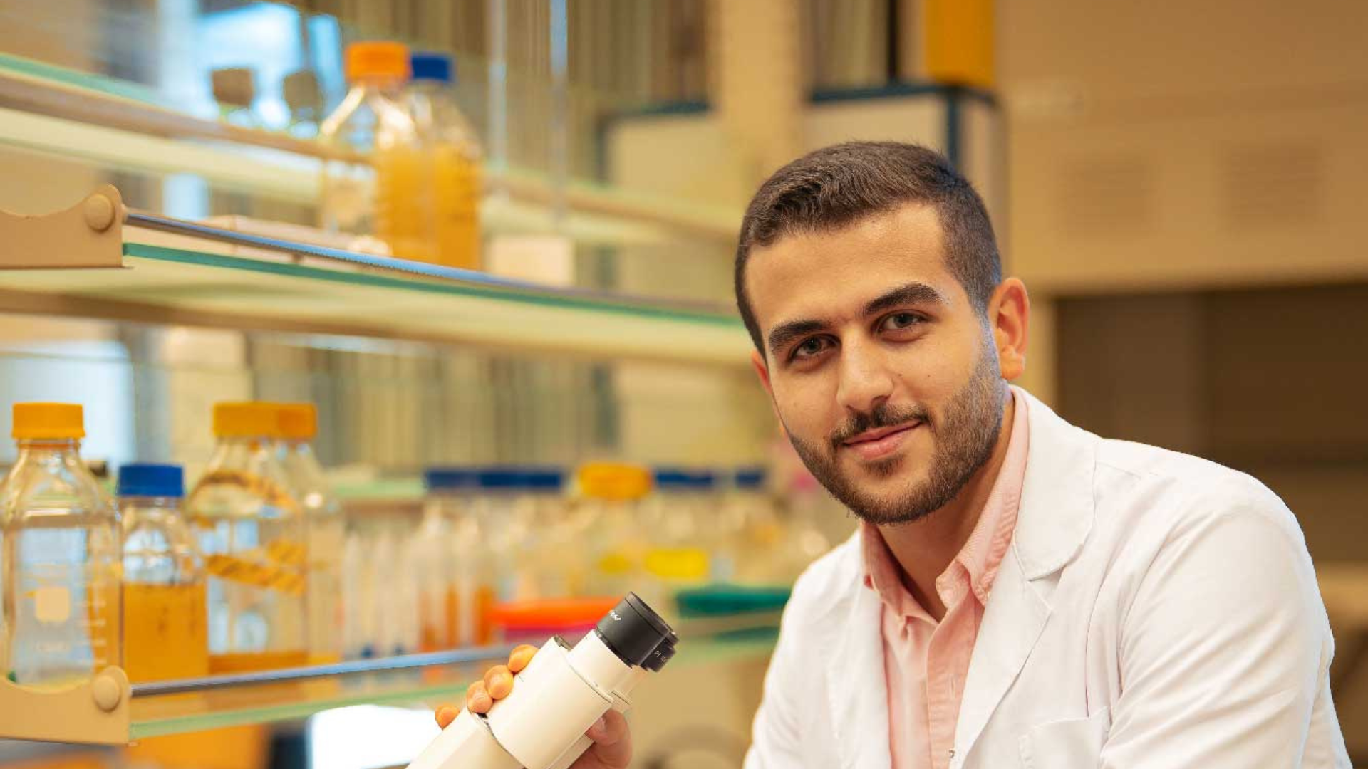 Yousef Taha in a labcoat with a hand on a microscope