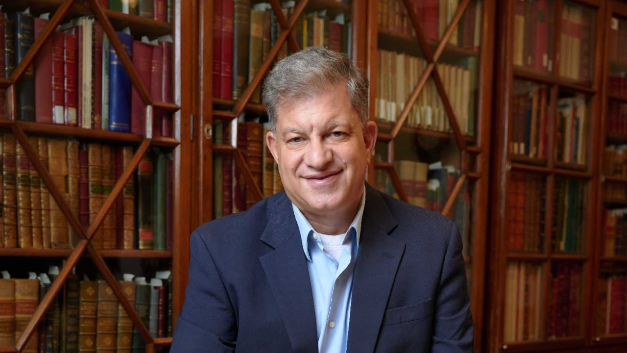 Man in blue suit stands in front of book shelves.