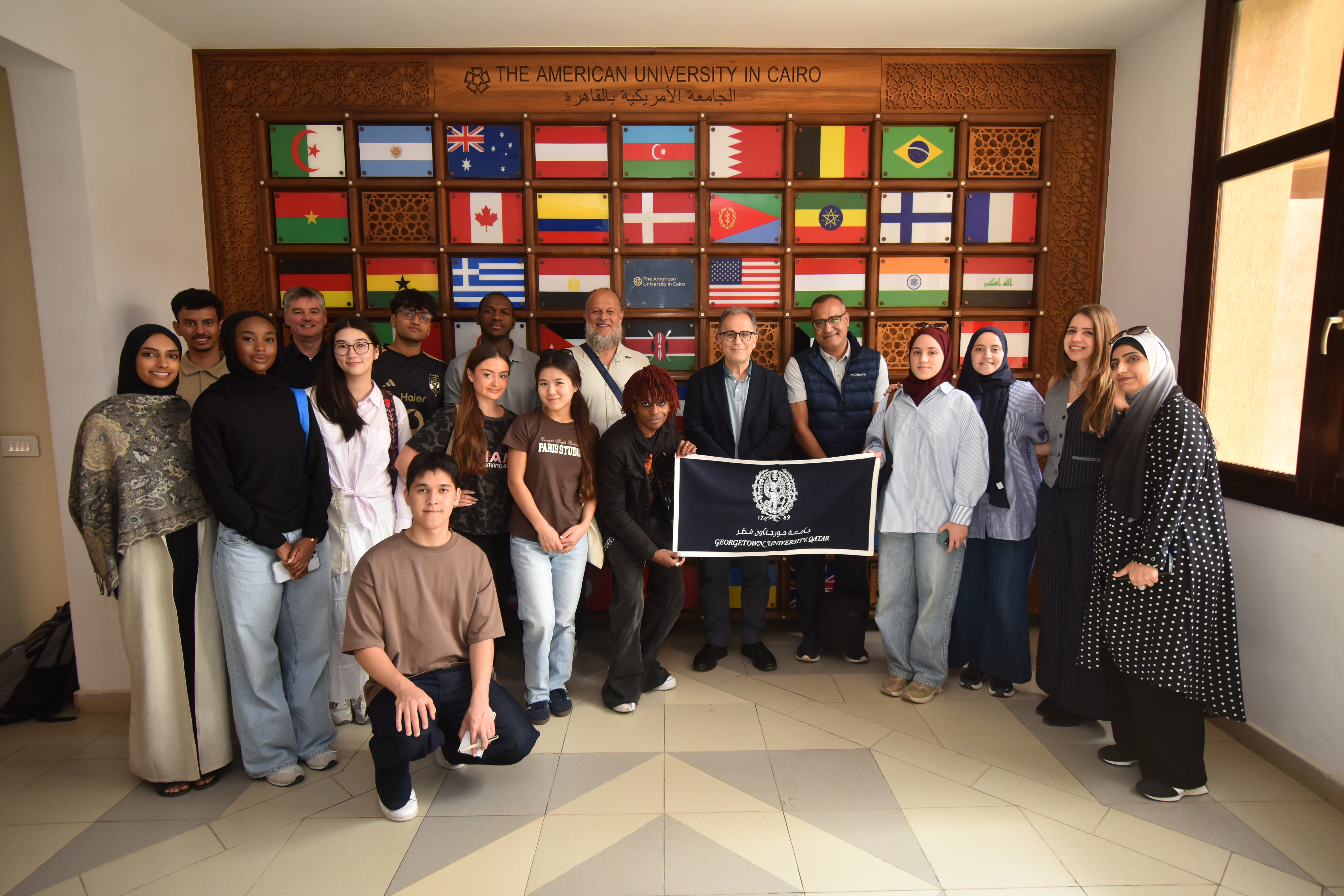 GU-Q students posing with President Dallal in front of many international flags