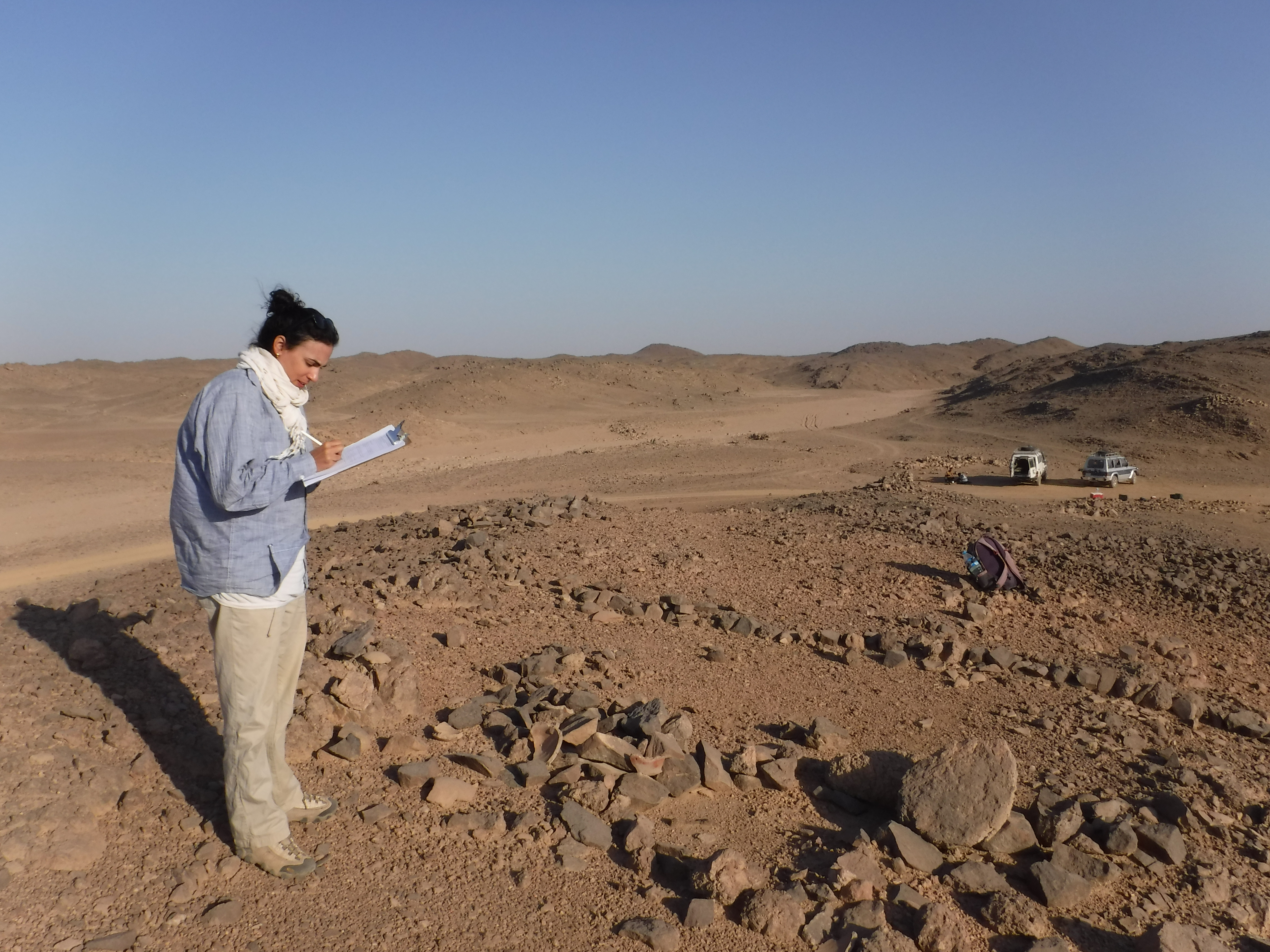 Meredith Brand standing in desert ruins holding a clipboard