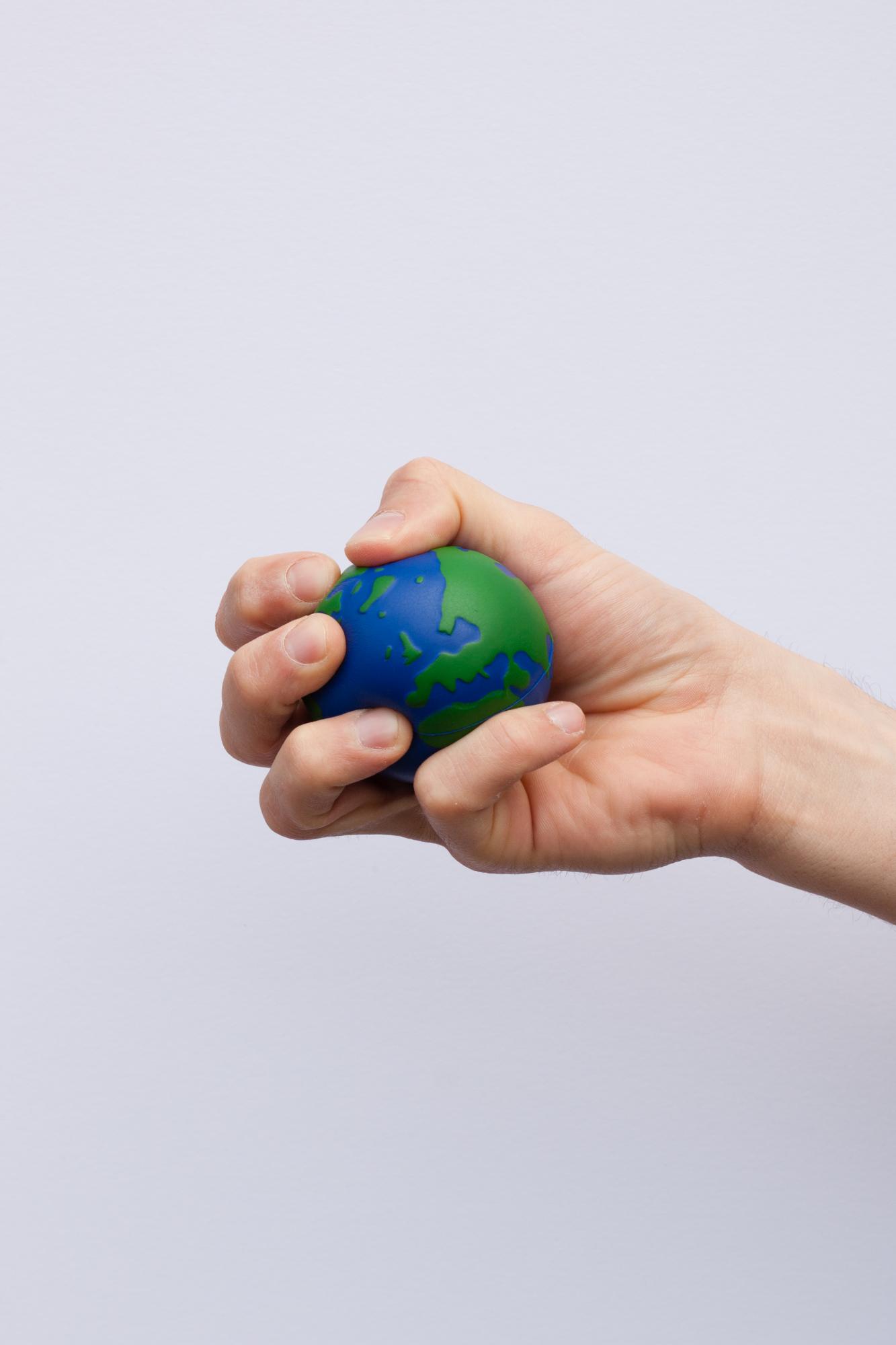 a hand catching an earth globe stress ball, the globe refers to the climate change challenges 