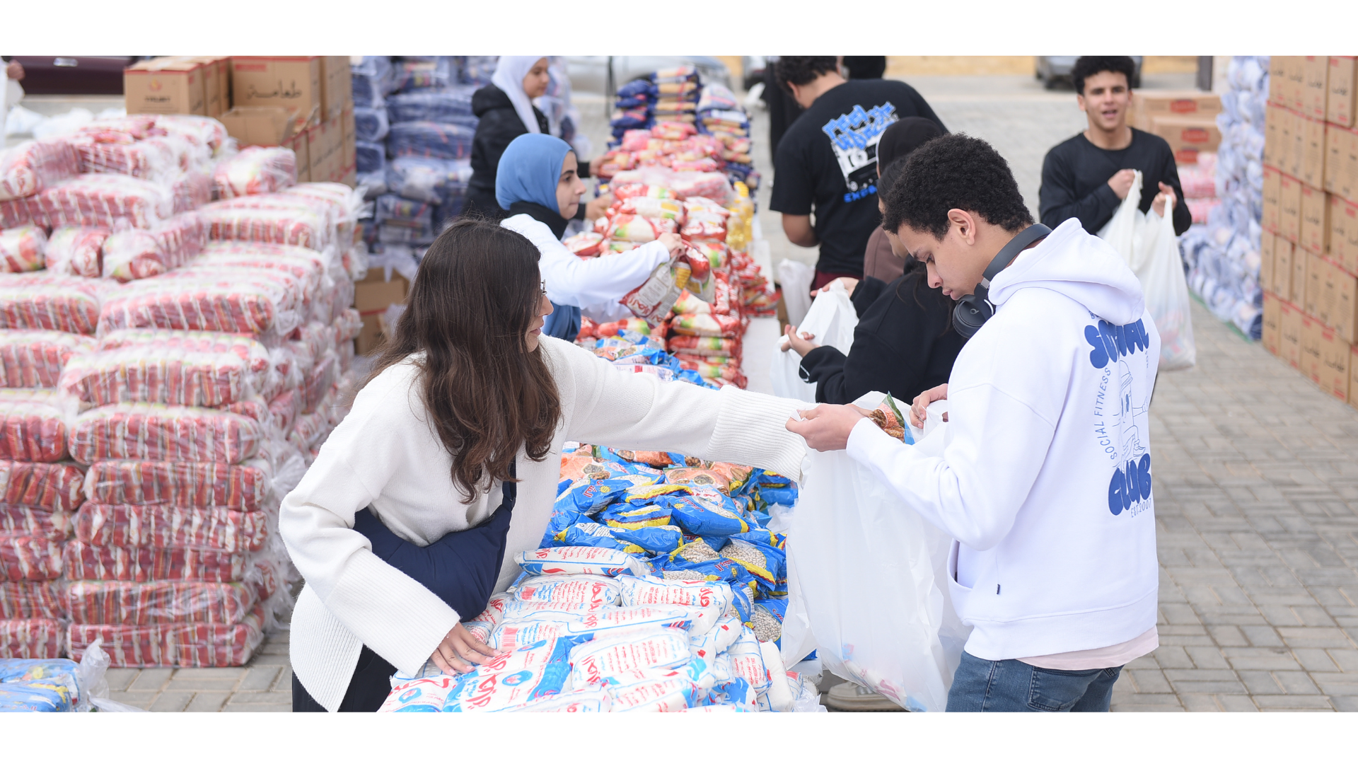 A young woman places a plastic bag of dry goods into the plastic bag of a young man