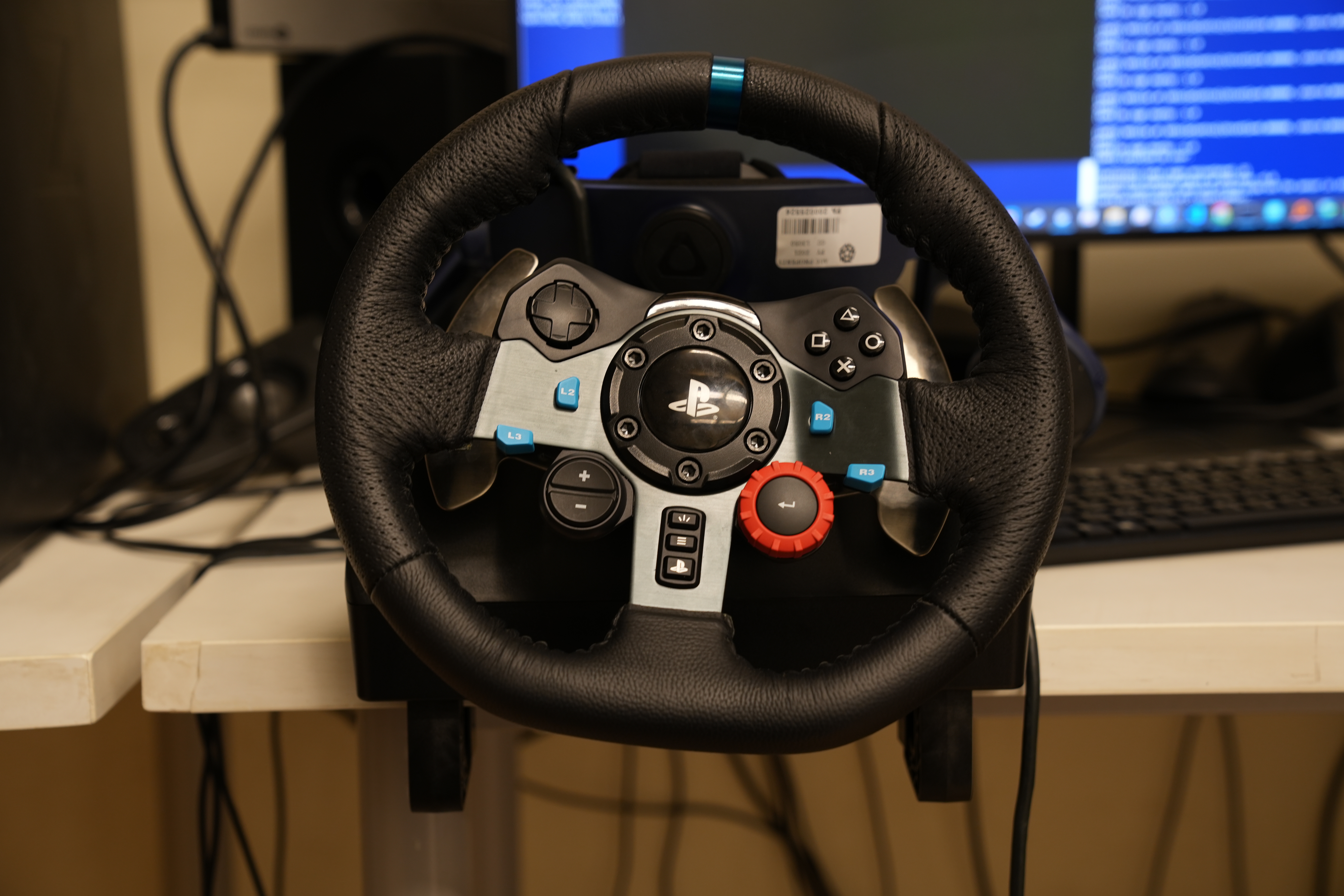 A Play Station controller with the grip of a steering wheel sits in front of a desktop computer