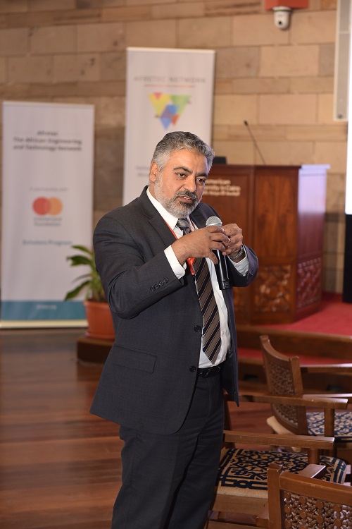 Professor Ismail stands and presents at the conference, speaking into a microphone and gesturing with his other hand