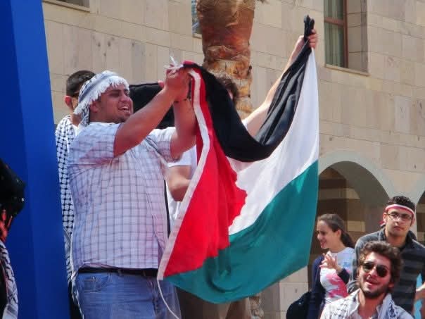 Mohammed Abuzaid holds a Palestinian flag in front of a crowd.