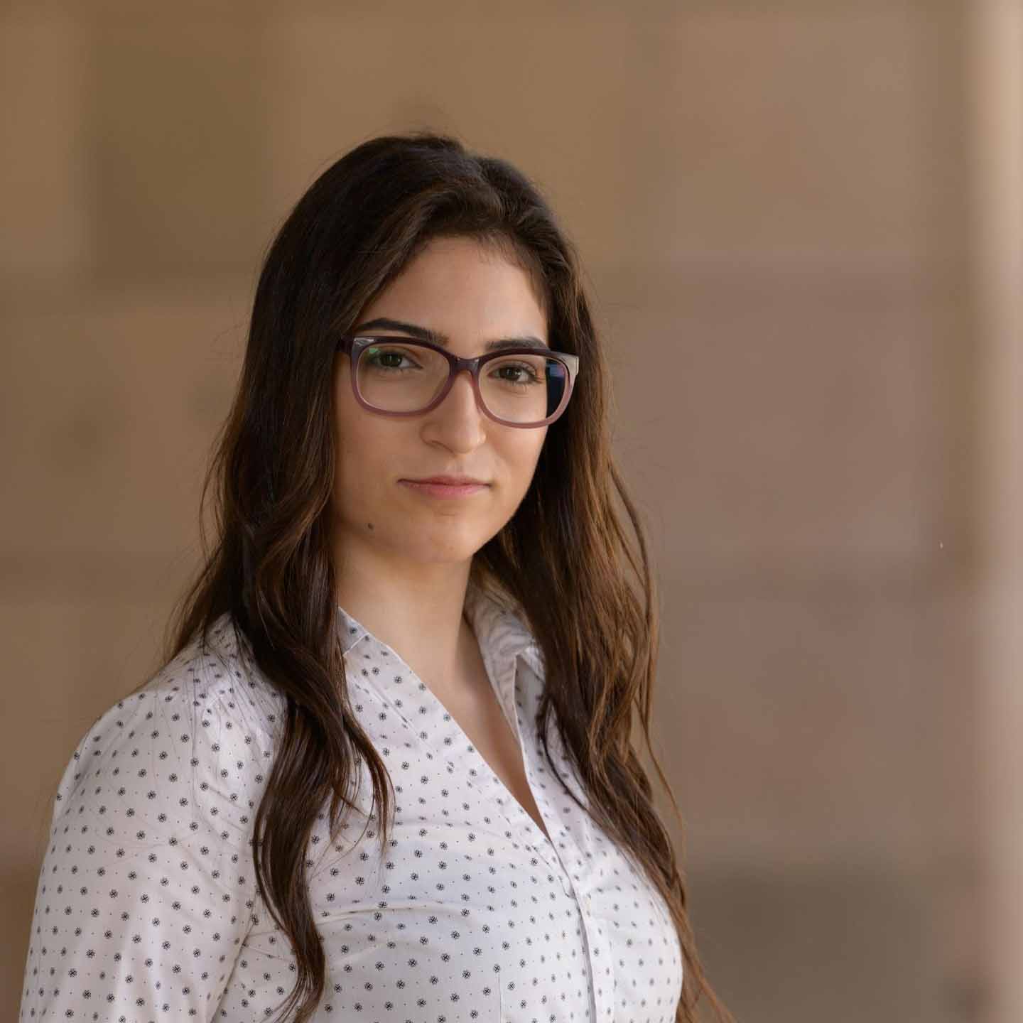 a girl with long brown hair wearing a white dotted shirt and glasses