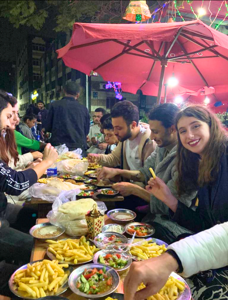 Carere sits at a table in the street with Egyptian food in front of her, sharing suhoor with her neighbors