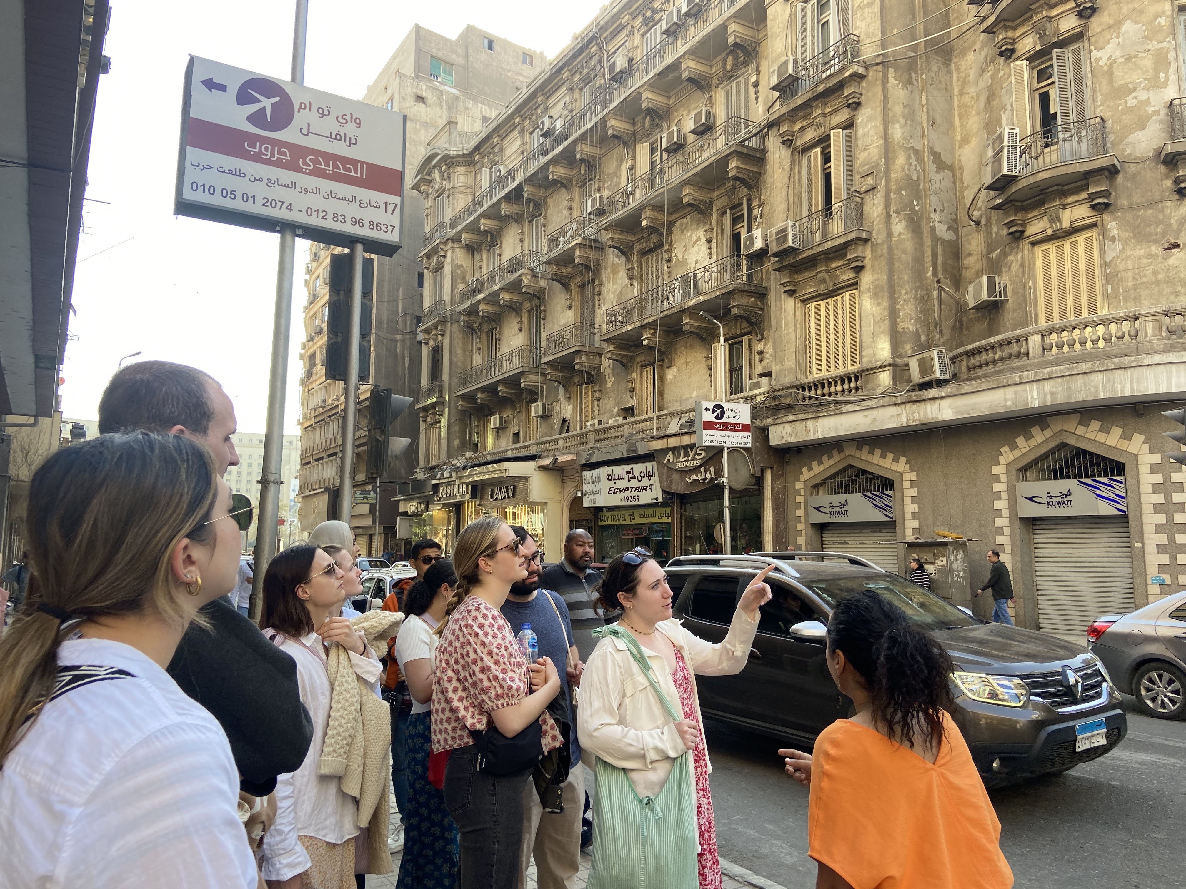 a group of people stand on the street in downtown Cairo, with a woman pointing at a building