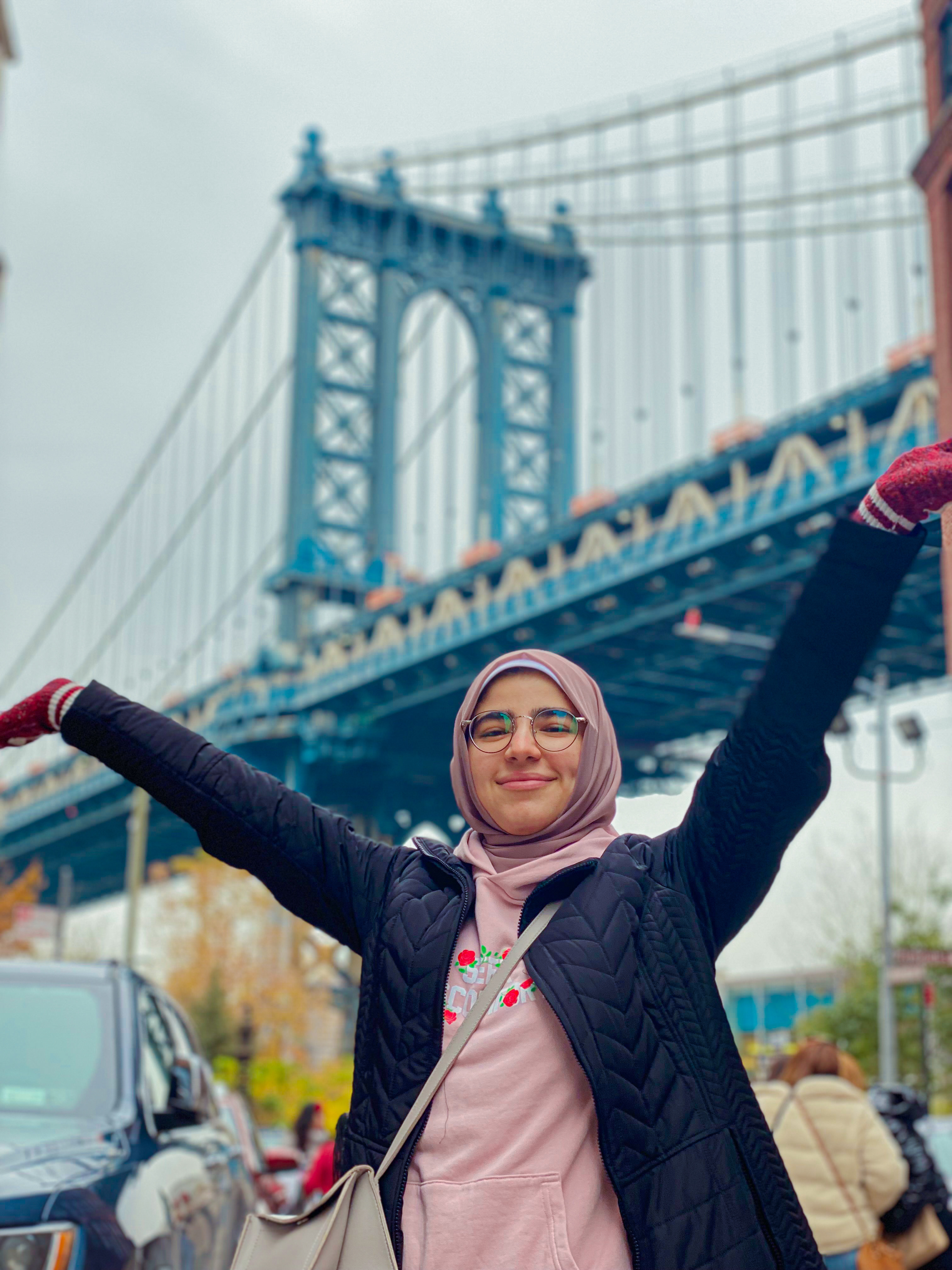 Menna Elzahar poses with her arms up in front of a bridge in the U.S.